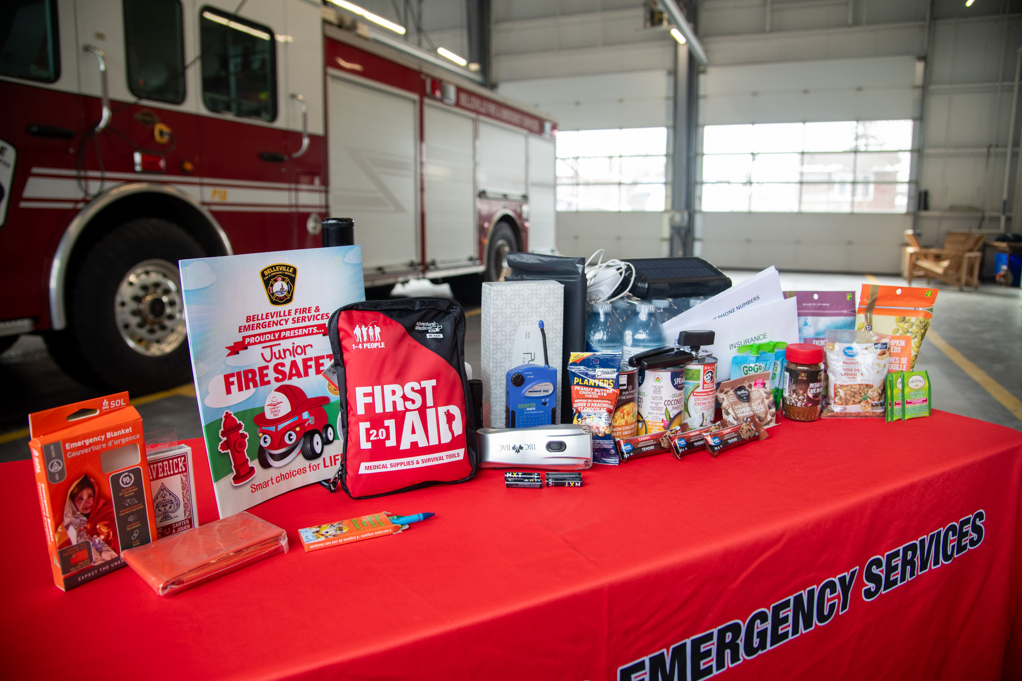 Assortment of items for an emergency kit including a first aid kit, heat blanket, snacks, walkie-talkies and activities.