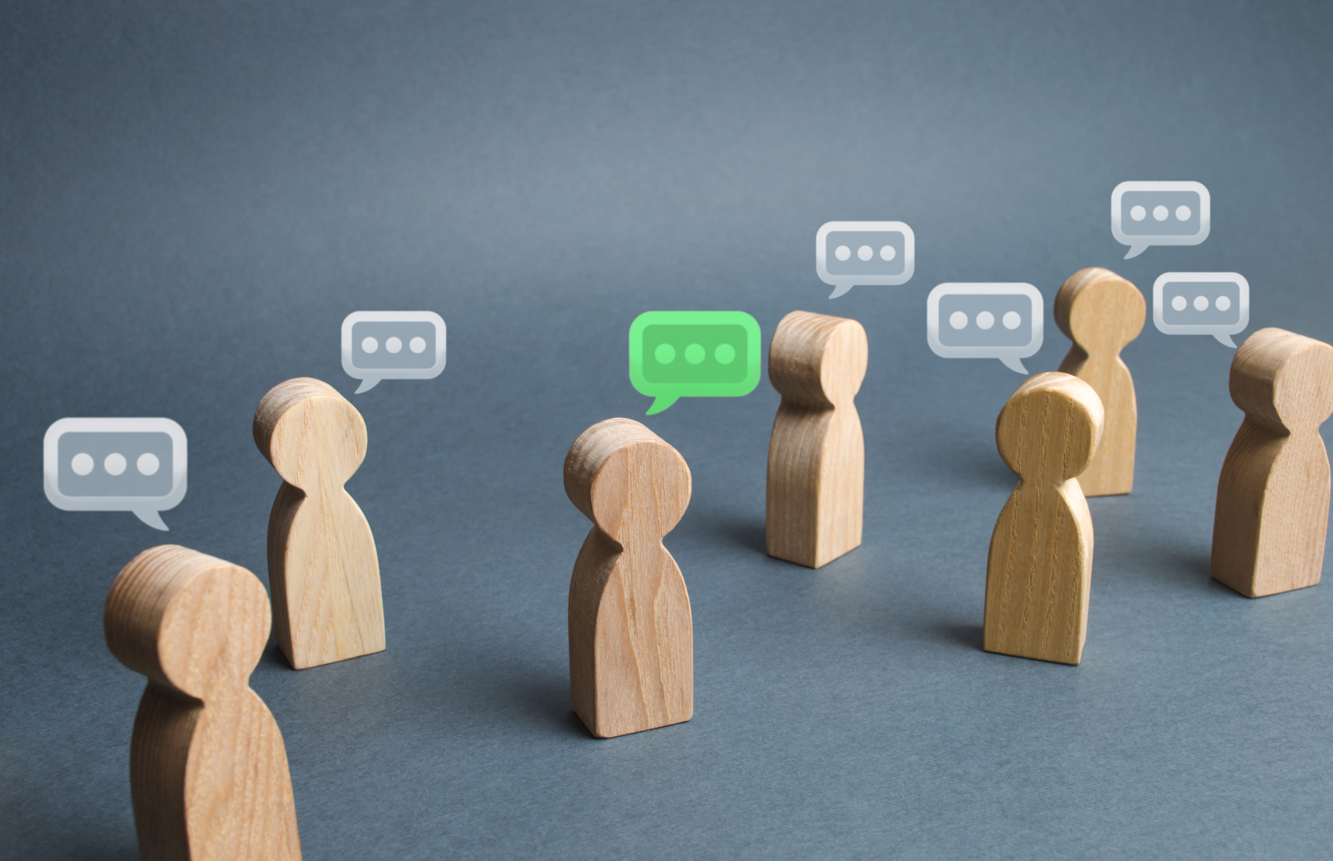 Wooden figurines arranged as a group with speech bubbles above them