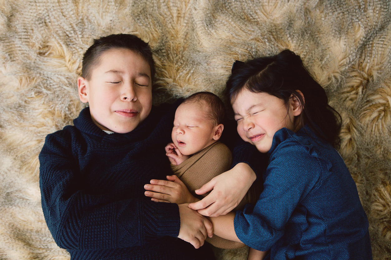 3 siblings - 2 children and a newborn - snuggling on bed