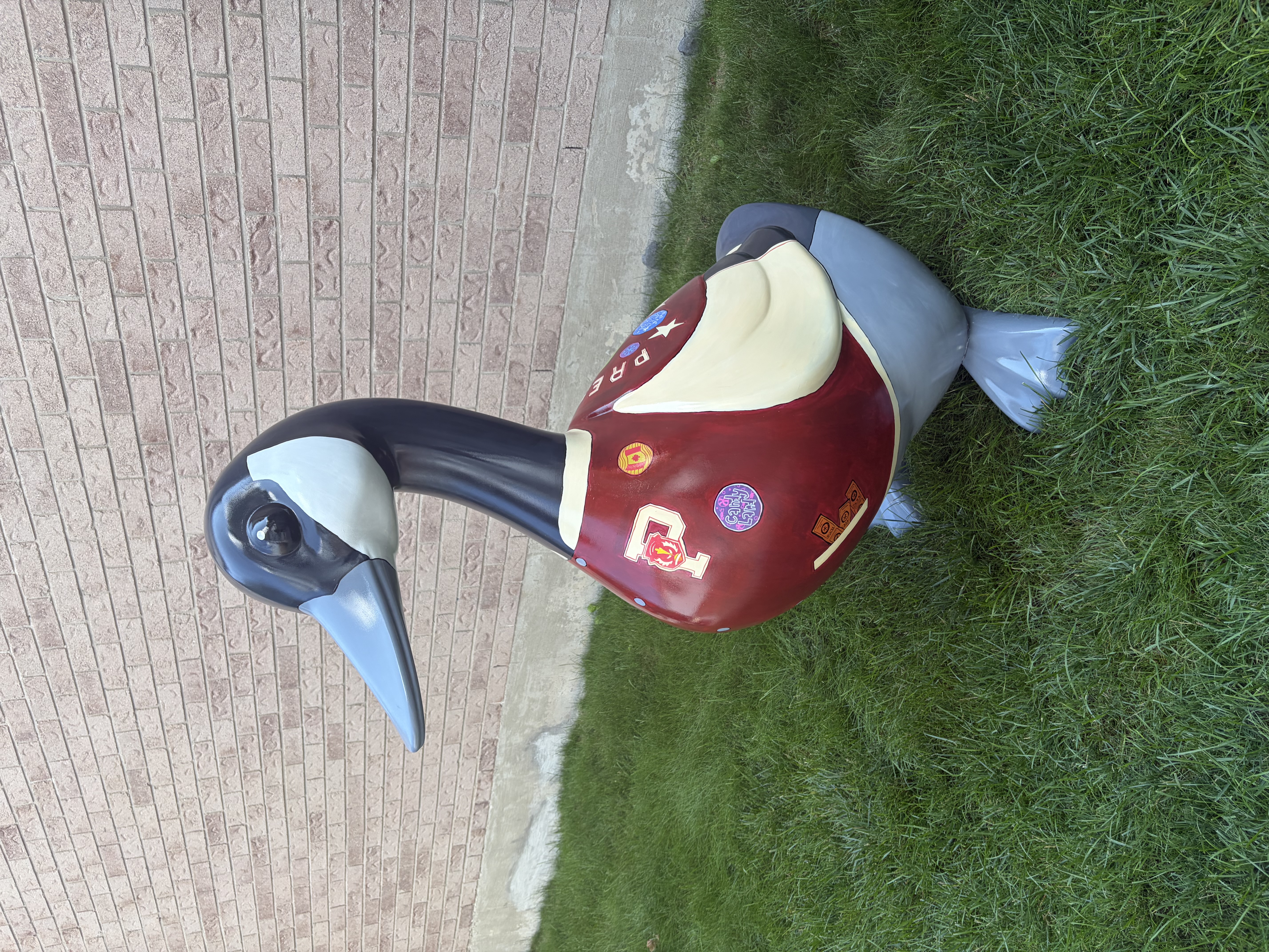 A 4.5-foot-tall fibreglass goose painted to look realistic with a grey body and black neck.  The goose is wearing a maroon and tan jacket featuring an emblem with the letter P and several small patches.