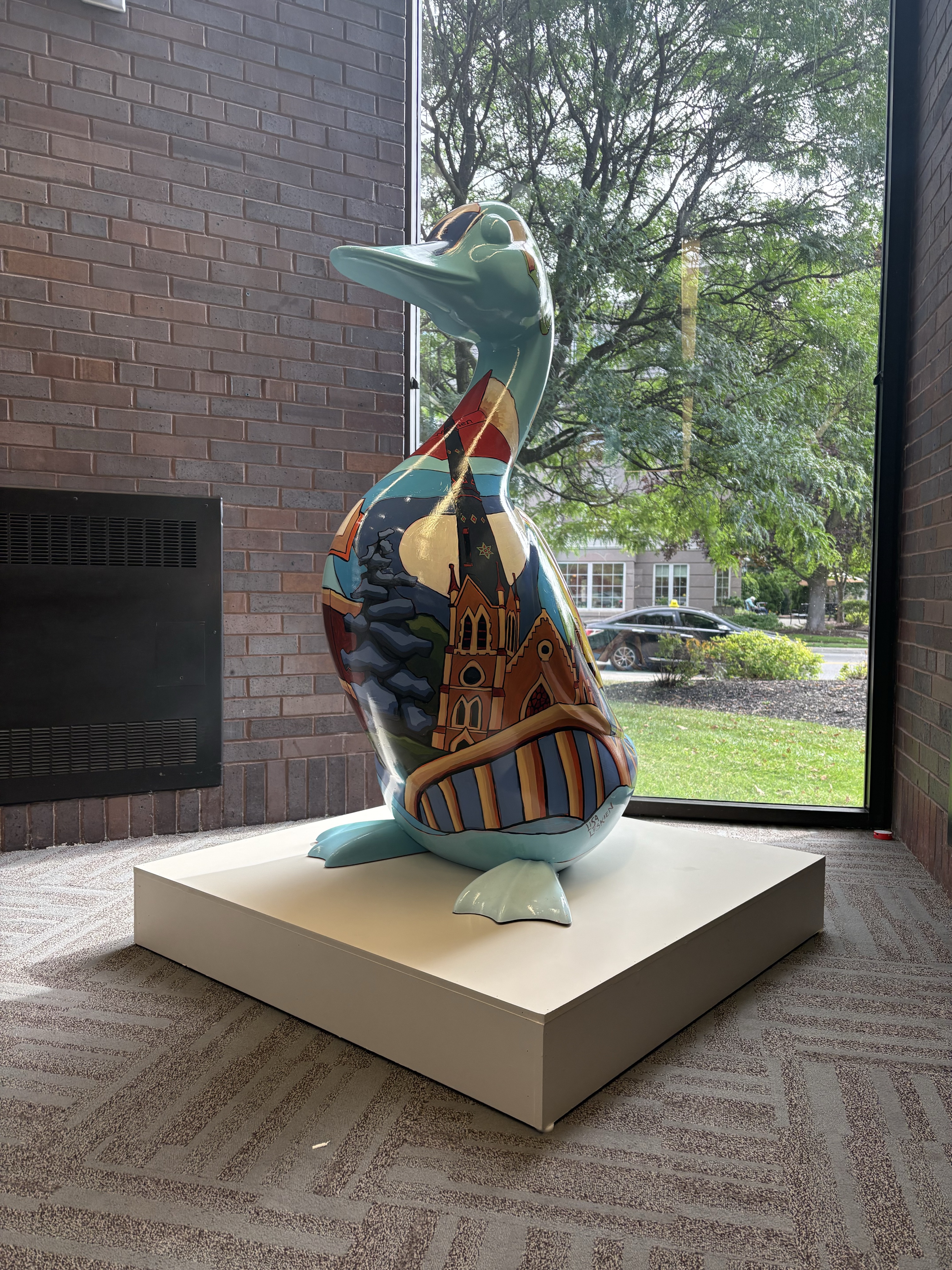 A 4.5-foot fibreglass goose on a white pedestal. The goose is painted with illustrations of architectural landmarks in Cambridge Ontario and books authored by prominent female artists