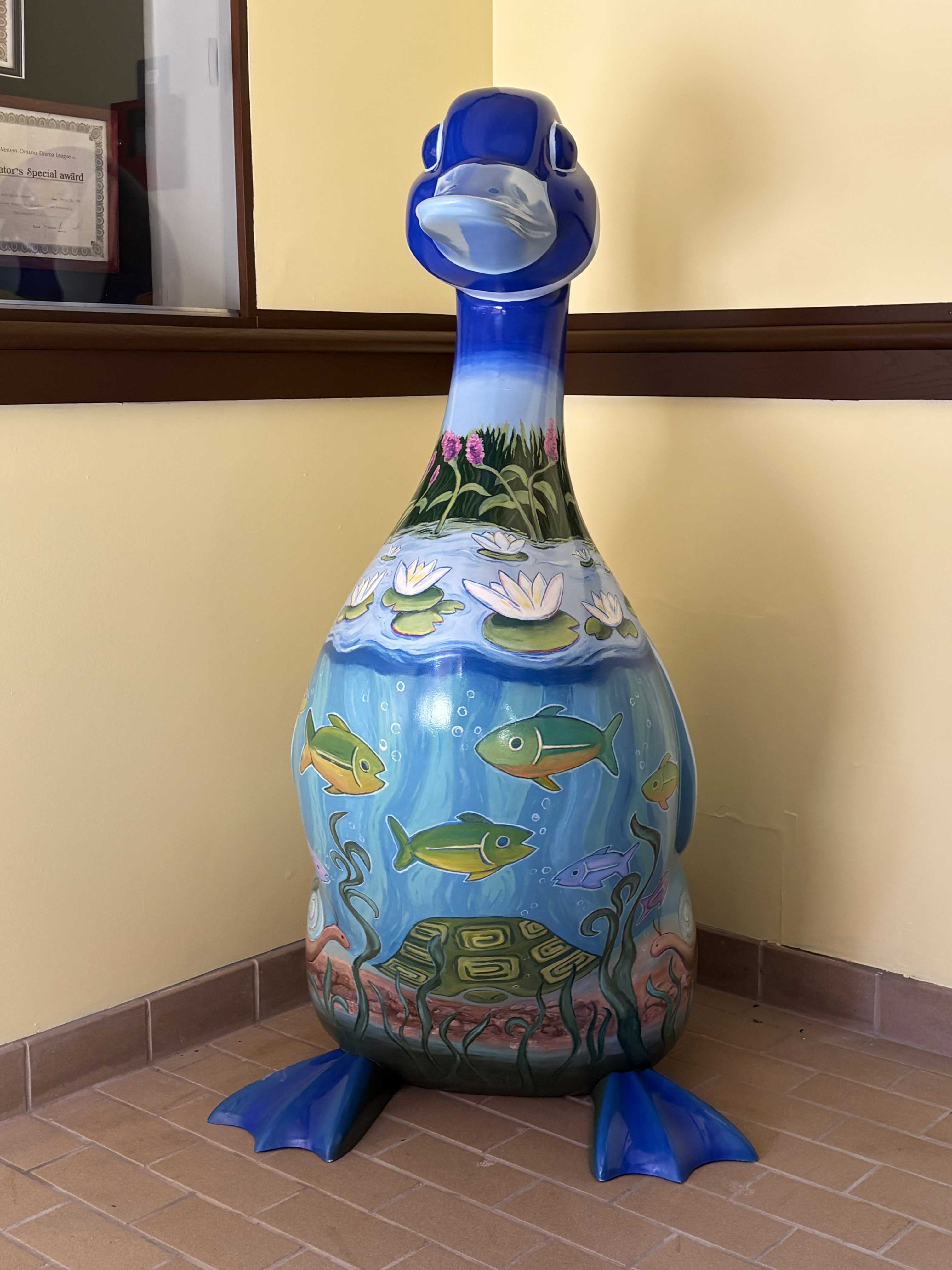 4.5-foot tall fibreglass goose decorated with a colourful painting featuring a wetland landscape of fish, water lilies and flowers below a bright blue sky.