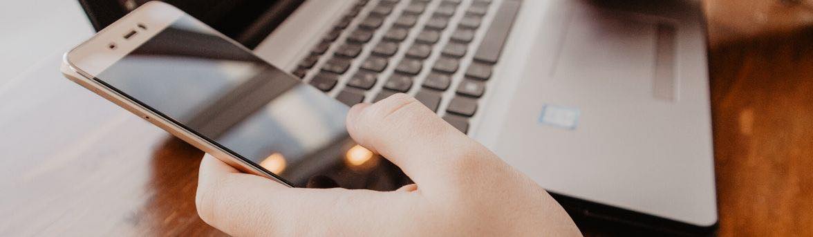a person holding a cell phone at a computer keyboard