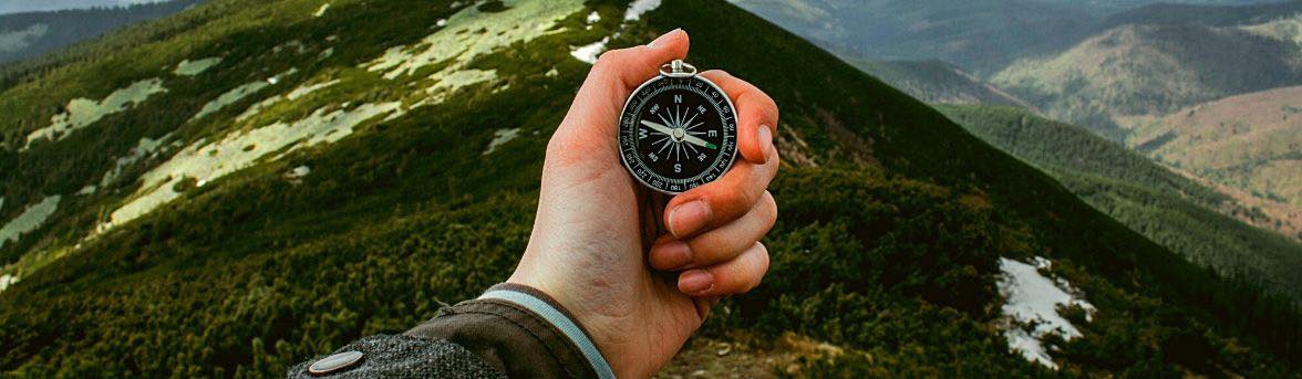 A hand holding a compass on a mountain range
