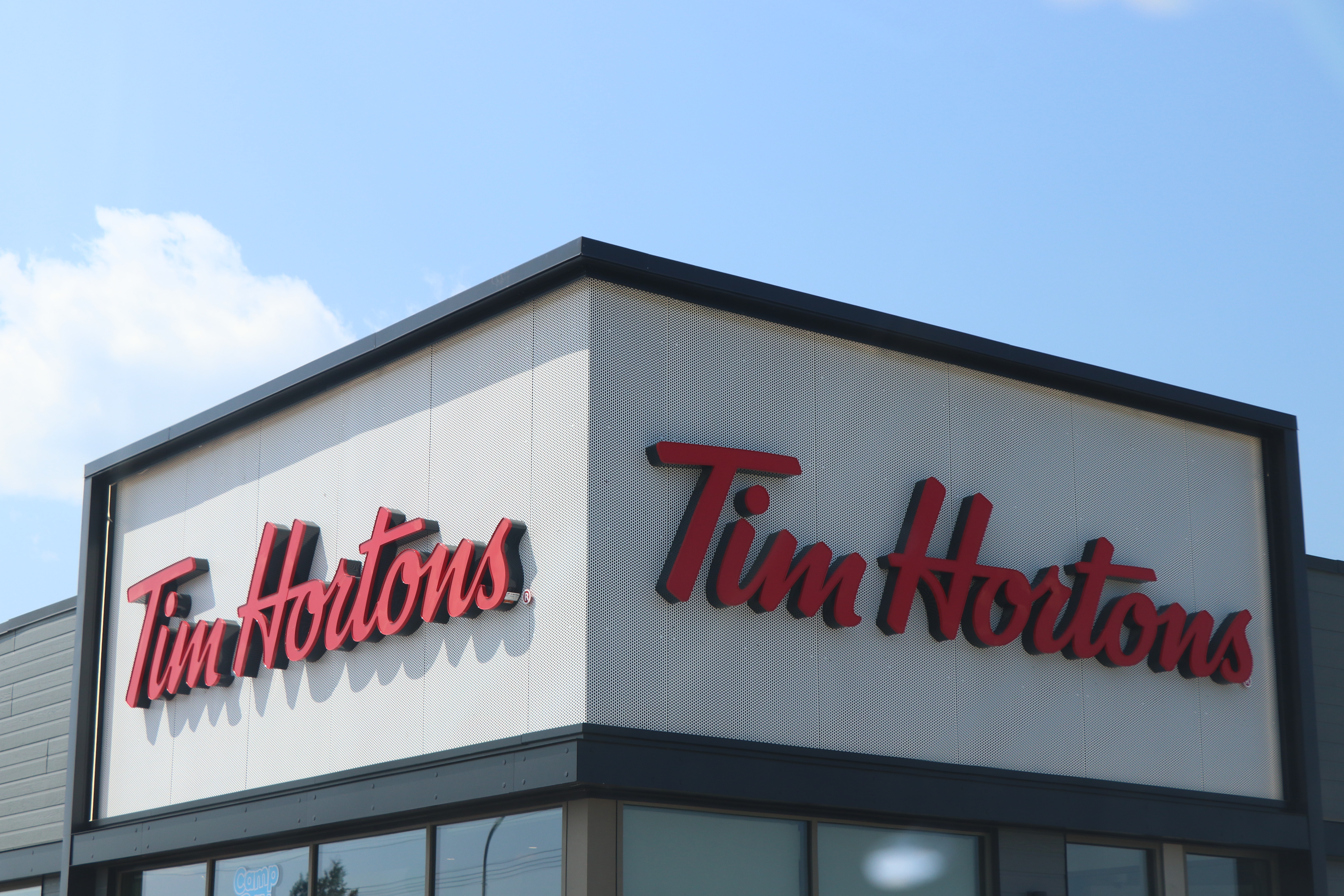 A Tim Hortons outlet with a prominent red "Tim Hortons" sign on a modern white building, captured under a clear blue sky.