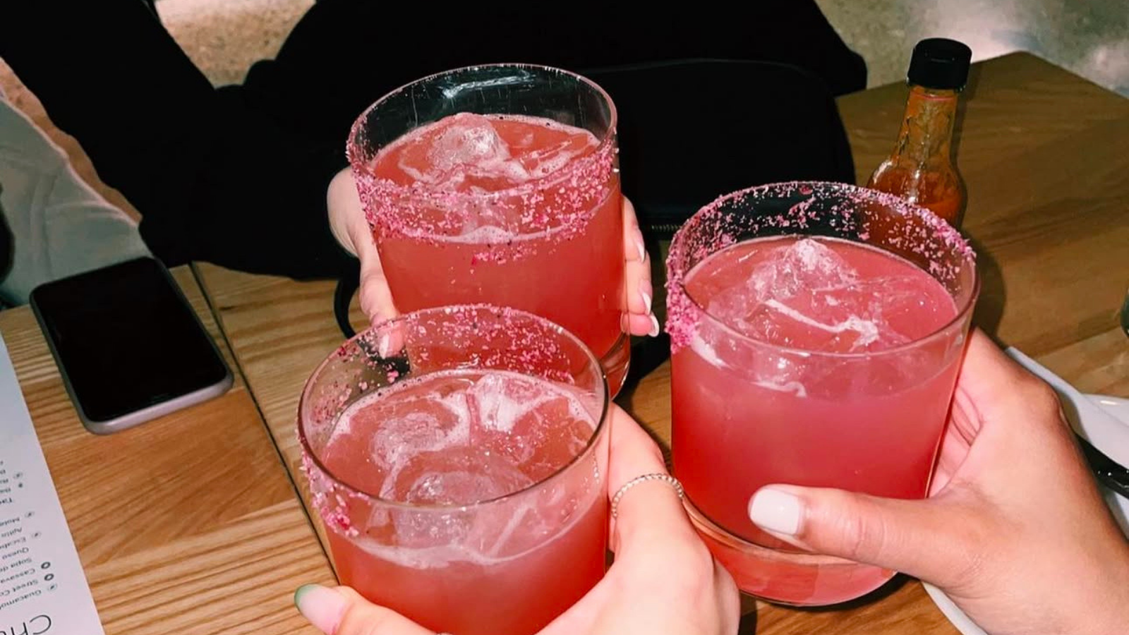 Three people gesturing cheers with margaritas at Chuuk in Pickering, Ontario