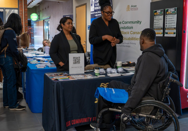 Photograph shows a busy indoor vendor fair with attendees visiting information booths and speaking with exhibitors.