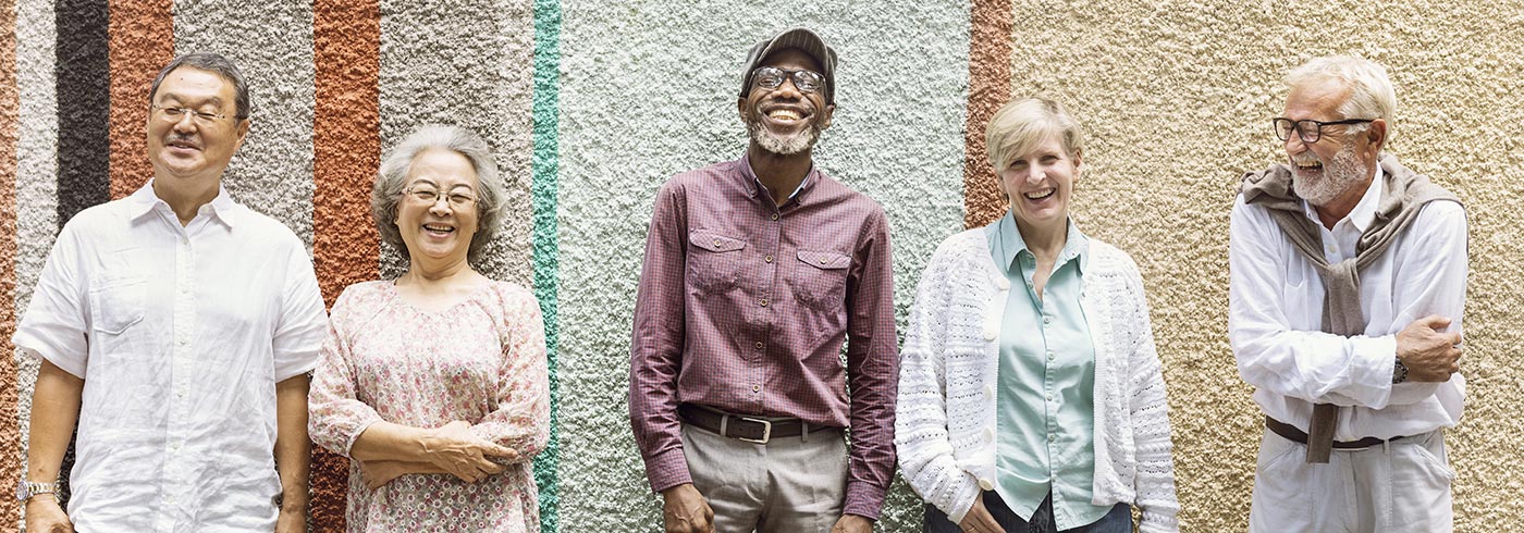A diverse group of older adults leaning against a multicolour wall.