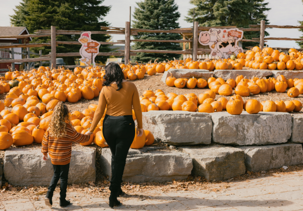 woman and little girl walk hand in hand to outdoor pumpkin display