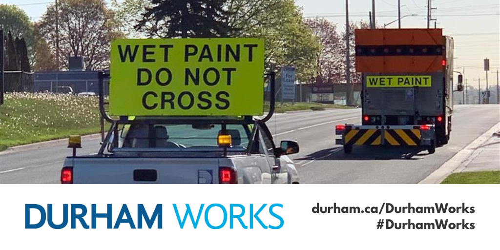 A photo of the back of two line painting vehicles with bright neon signs reading Wet Paint Do Not Cross and Wet Paint with a Durham Works logo banner and text reading durham.ca/DurhamWorks #DurhamWorks