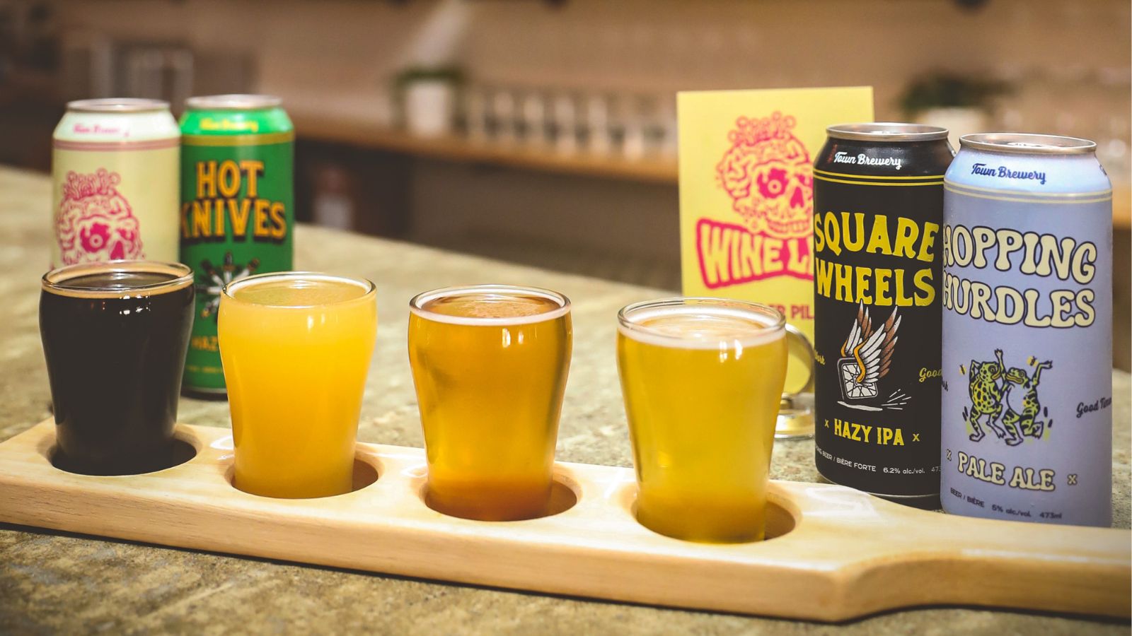 Image of a tasting flight of beer on a wooden paddle with cans of beer on either end of it