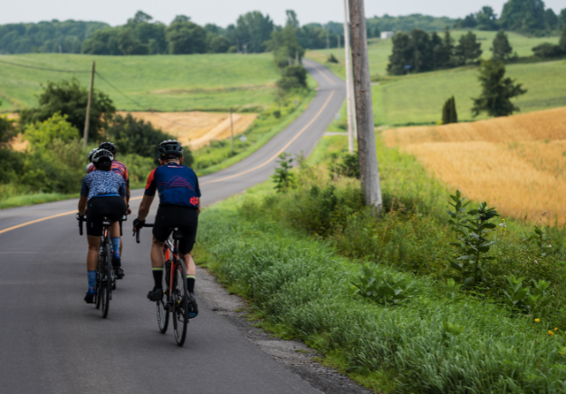 three cyclists ride on an empty rural road