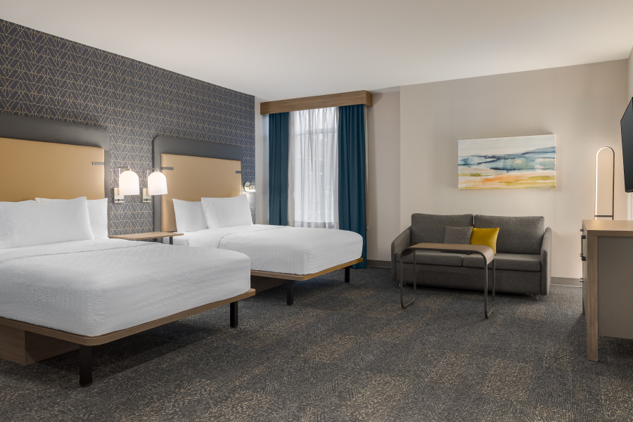 Hotel guest room with two queen beds, a grey couch and desk