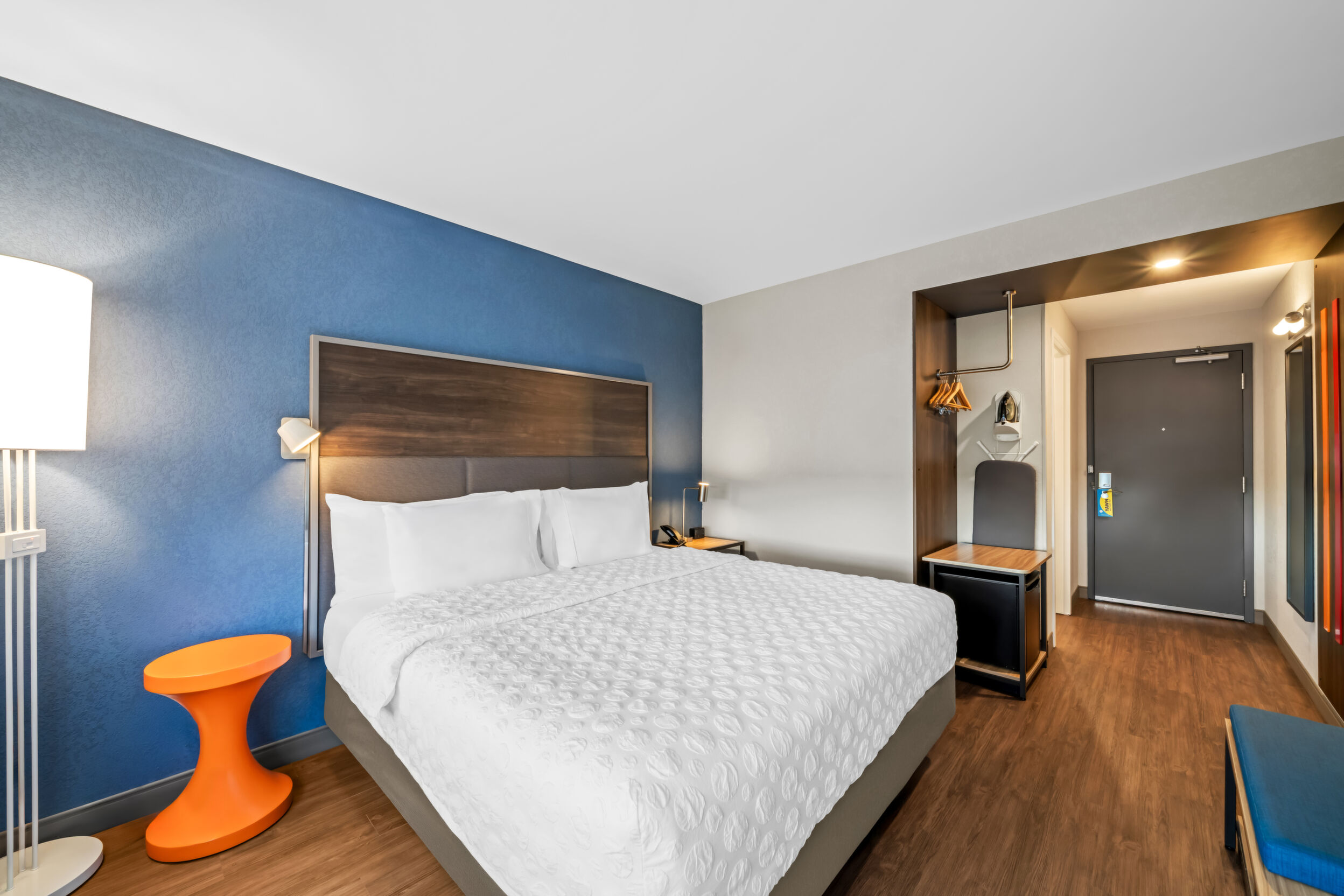 Hotel guest room with king bed, mini fridge, ironing board and orange side table