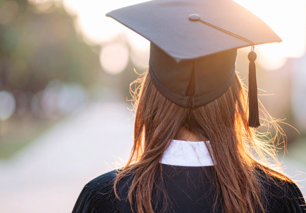 A graduate student wearing their cap and gown, facing the sunshine.
