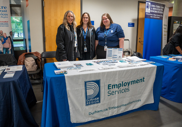 Durham Region Employment Services information booth with three staff standing at the table with. e blue-and-white tablecloths and brochures.