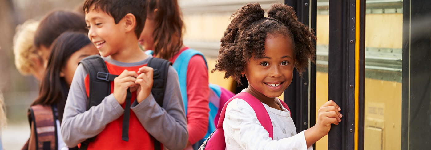 A group of children with backpacks happily boarding a school bus.