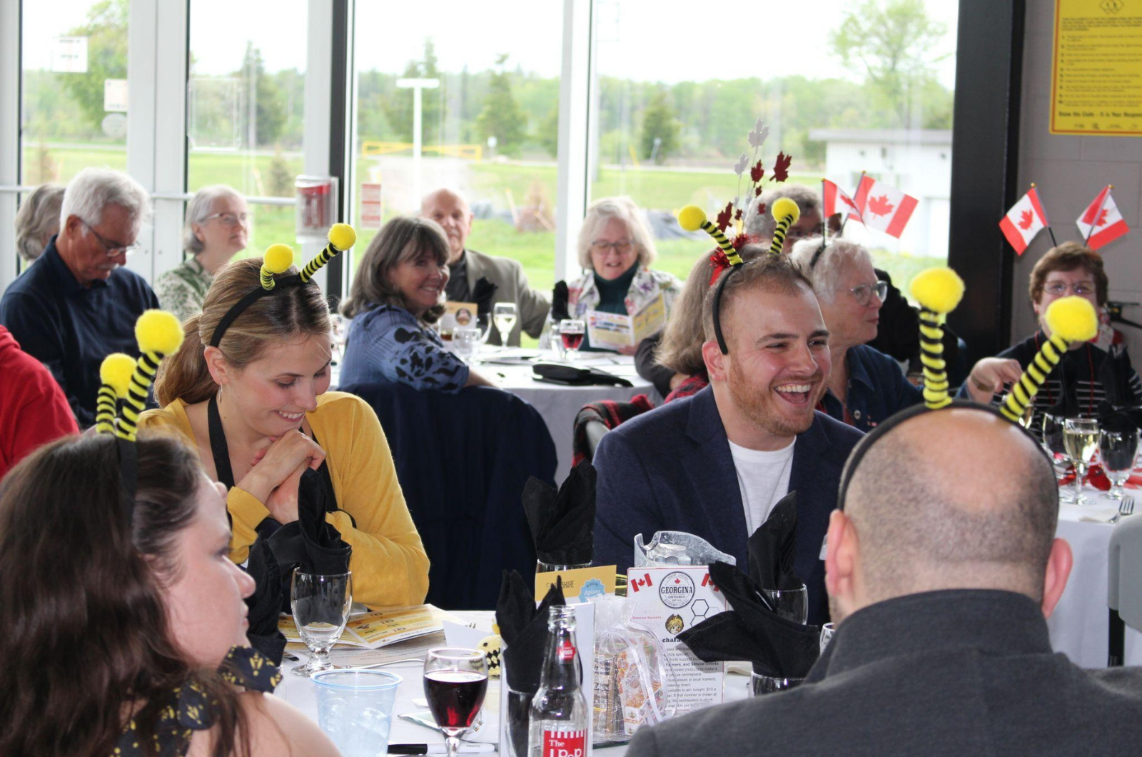 people wearing bee headbands laughing, while sitting at a table at a spelling bee