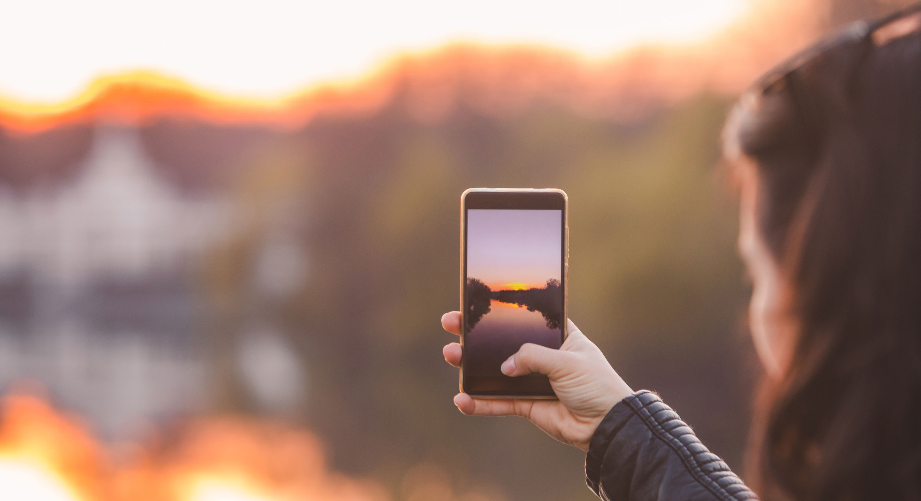 Person holds up a smart phone taking a photo of a sunset