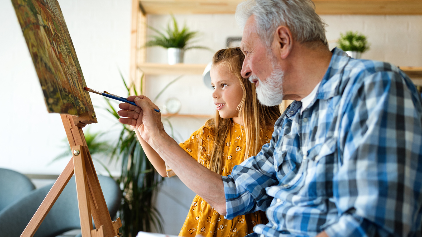 Senior man and young girl painting on a canvas