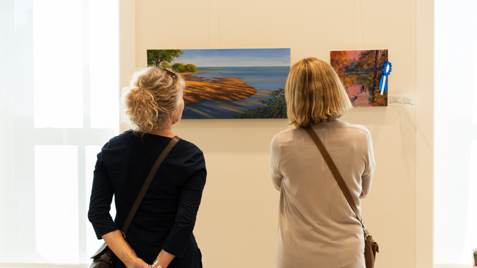 Two attendees of the Show & Sale look at the painting on the wall from the Great Migration Paint Out 2024