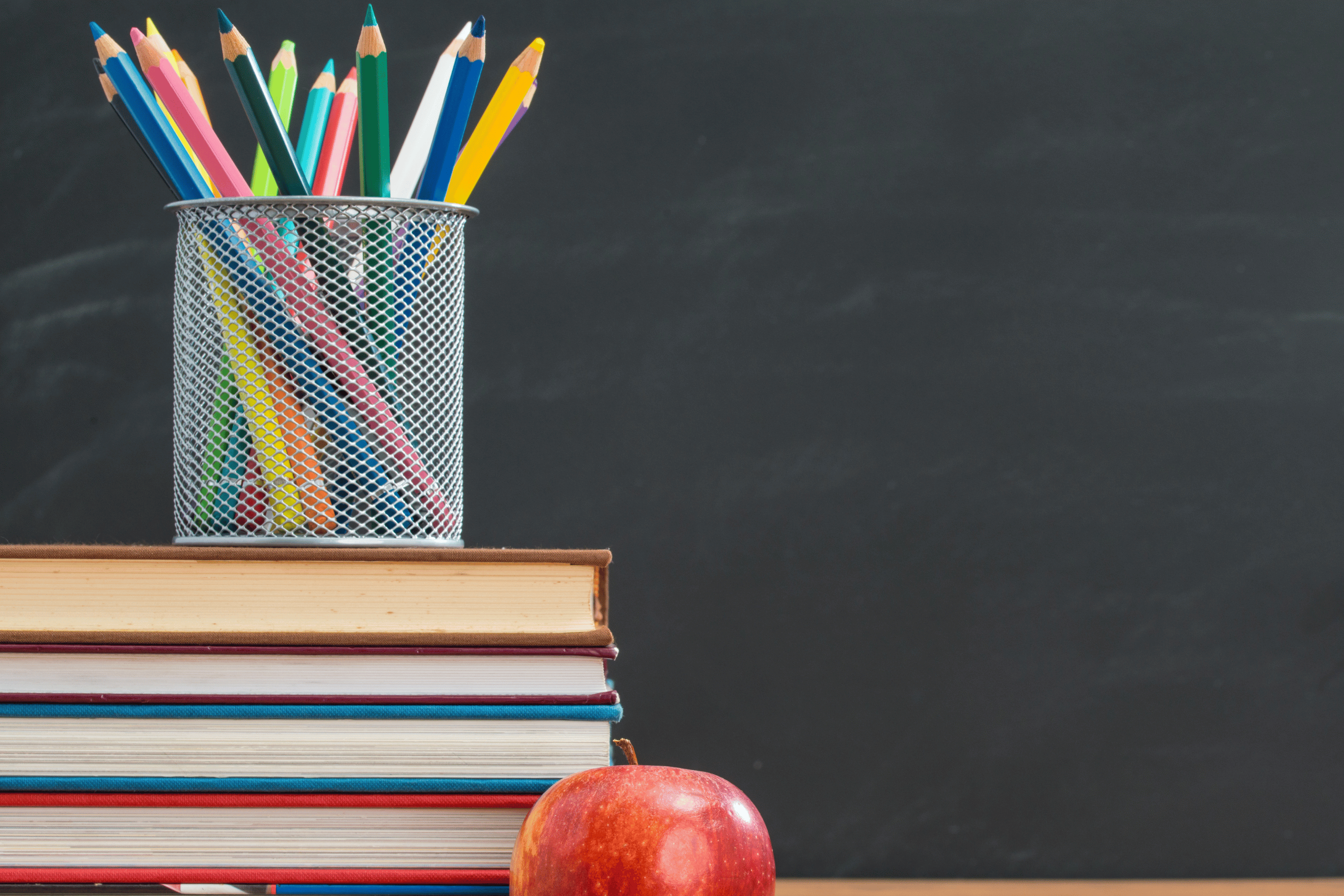 Pencil crayons, books and an apple on a desk