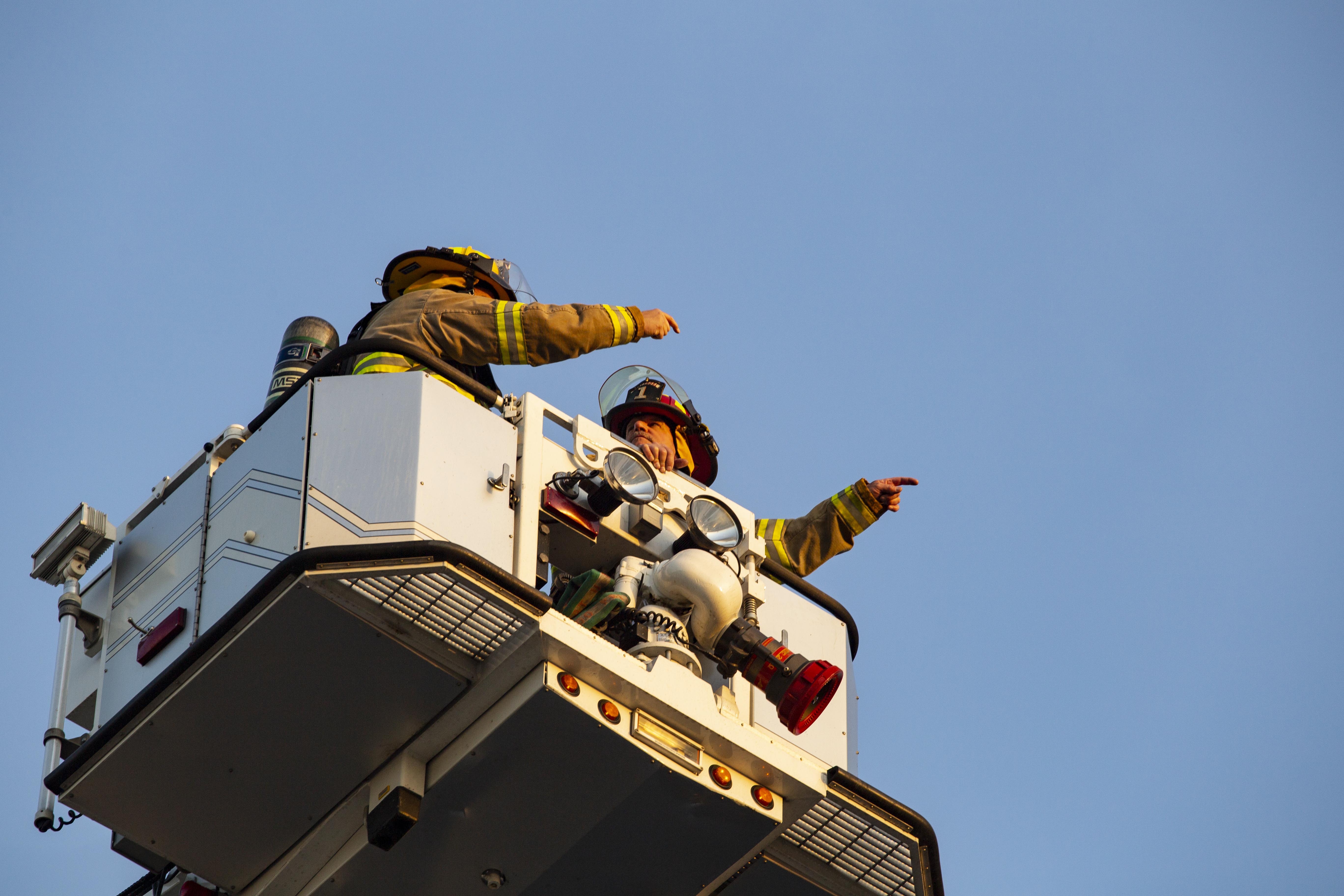 Lakeshore firefighters on a lift truck pointing in the sky.