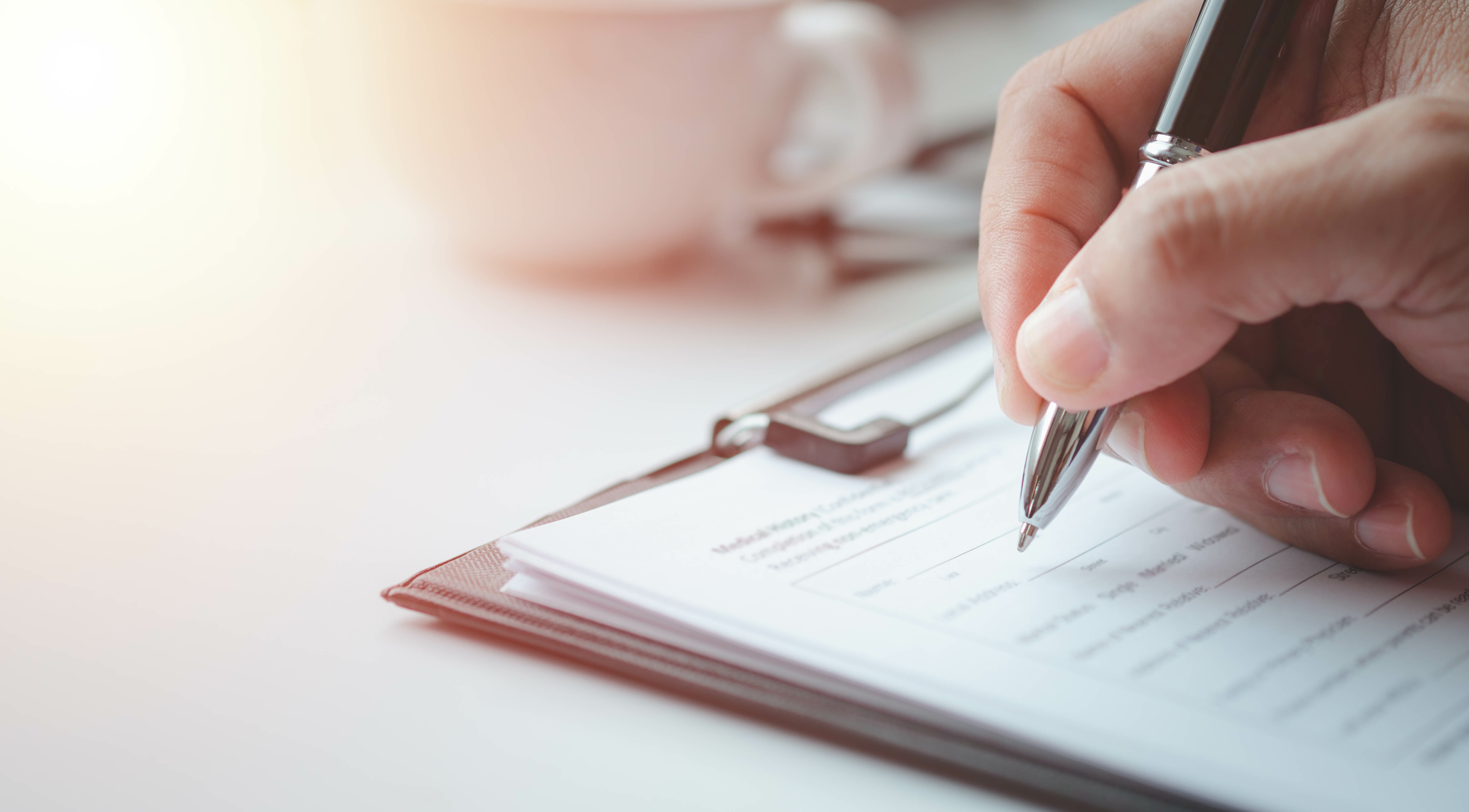 Hand filling out a paper form with a pen.