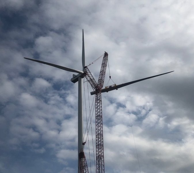 A crane is lifting equipment near the blades of a wind turbine against a cloudy sky.