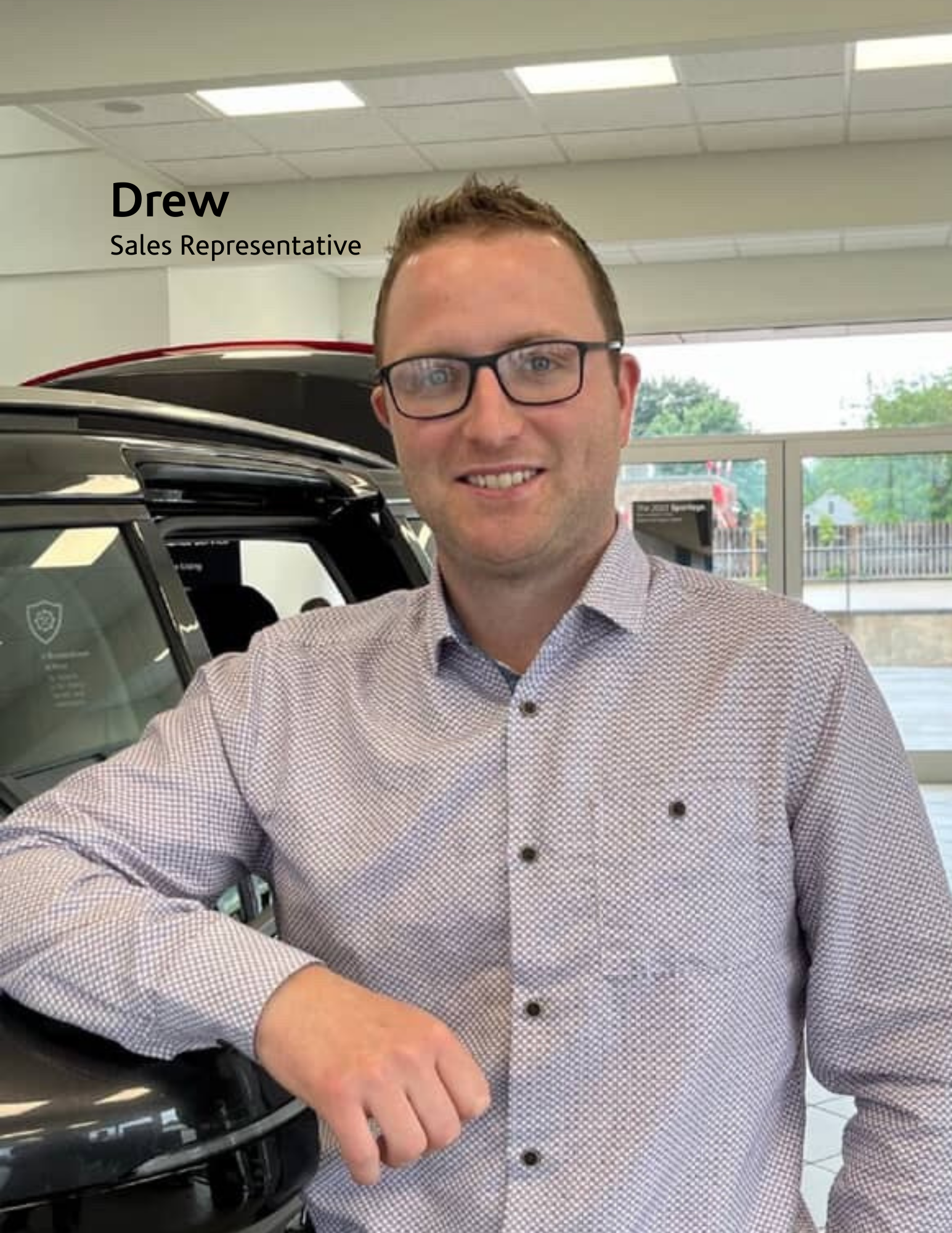man posing beside a car inside a dealership