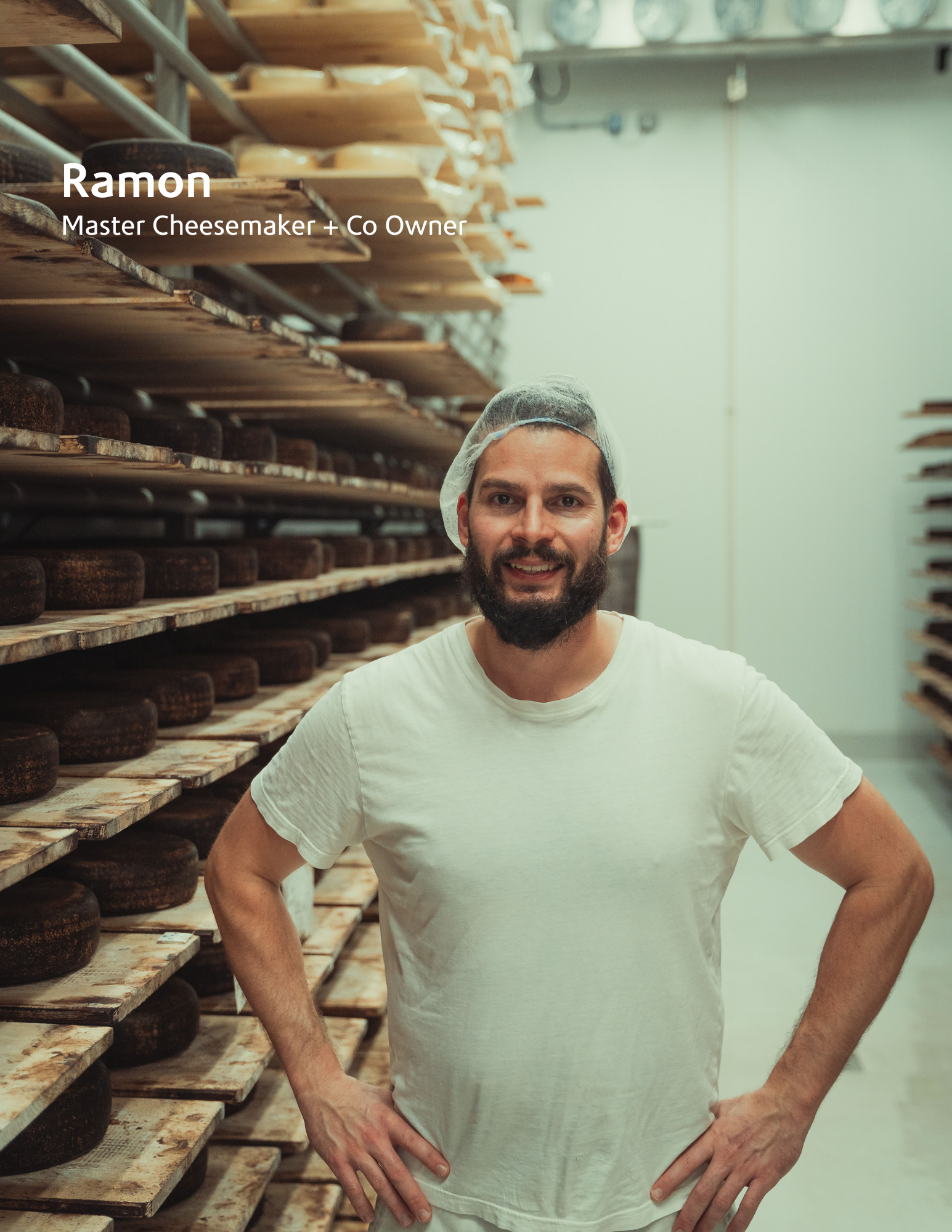 cheesemaker standing in a room filled with shelves of cheese wheels