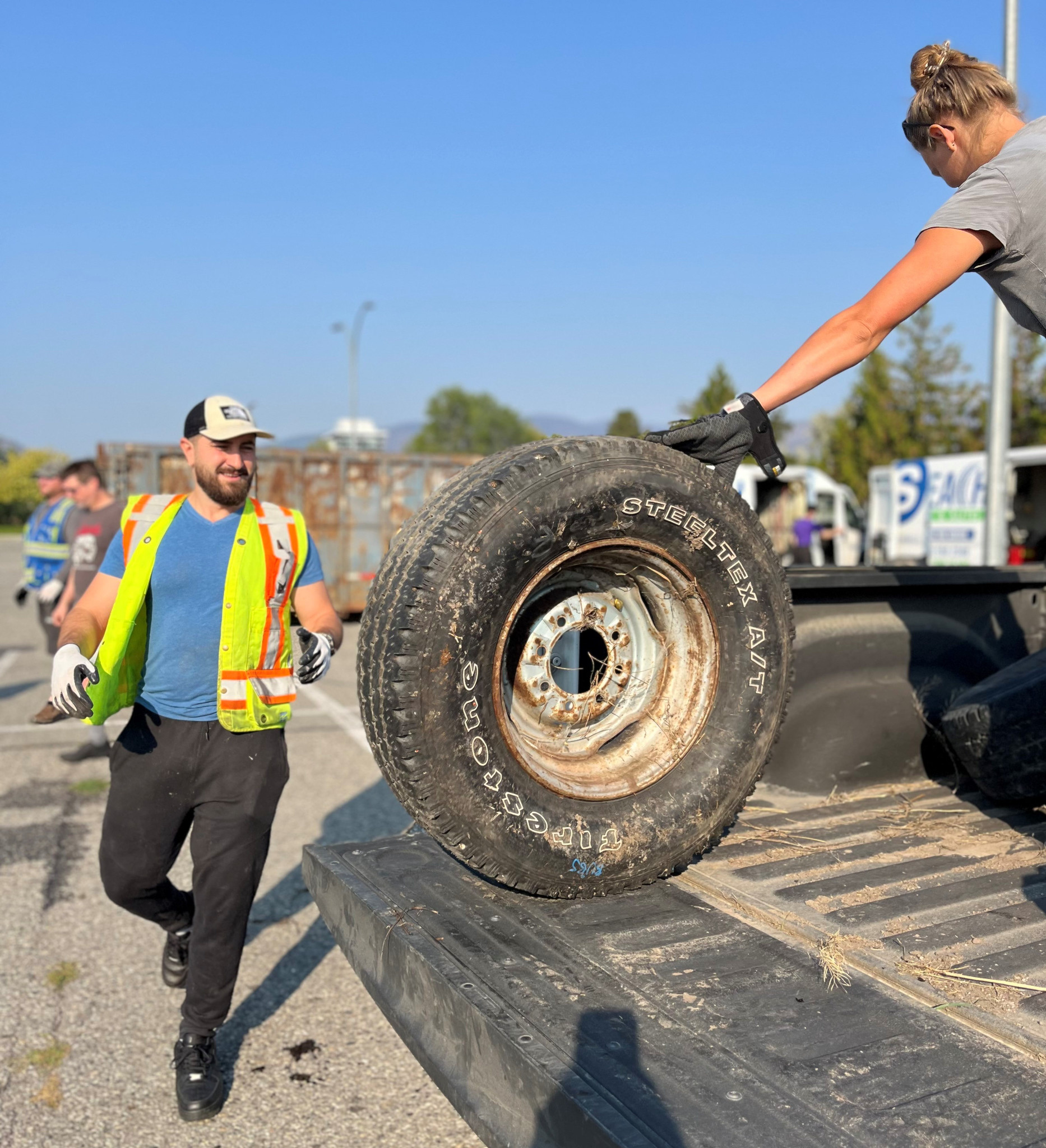 Worker in safety vest accepts tire handed by a woman on the back of a pick-up truck 