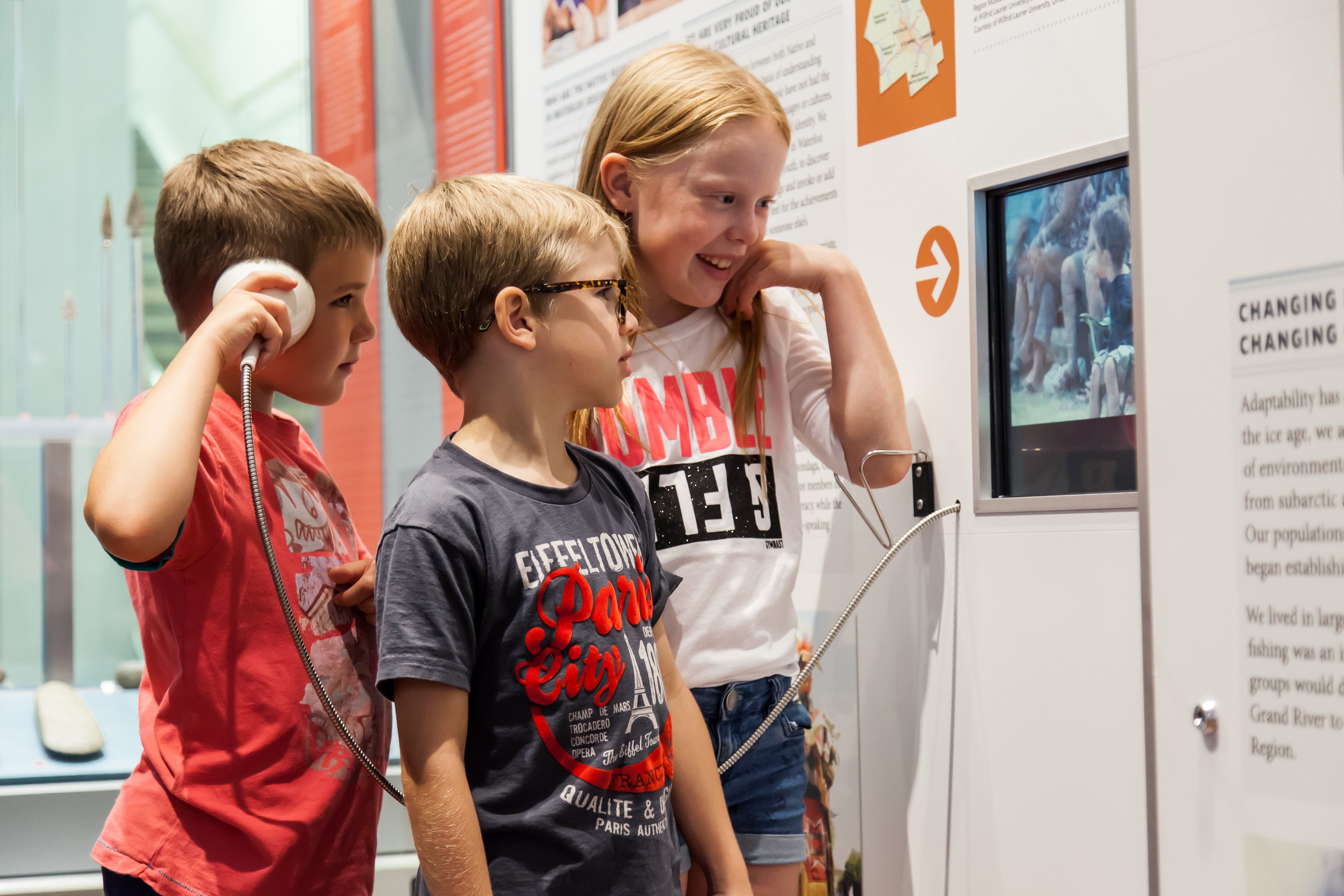 three young children listening to video player in museum