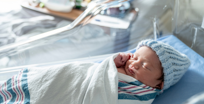 a newborn baby in a hospital crib, wrapped in a blanket with a hat on. 