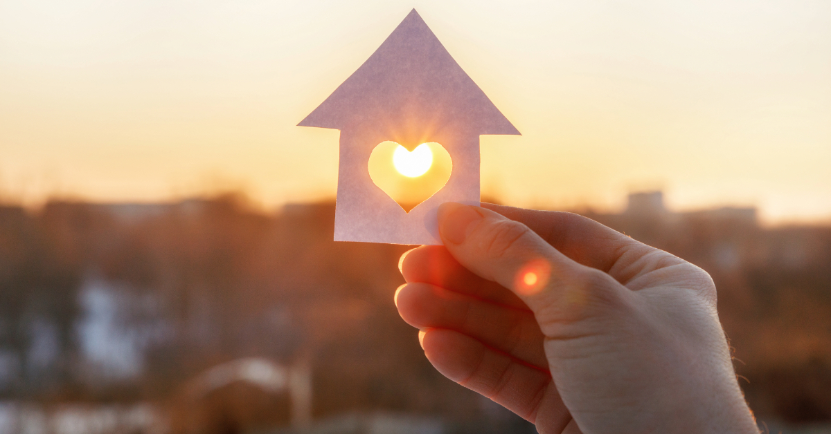 A person holds up a cut out image of a home.