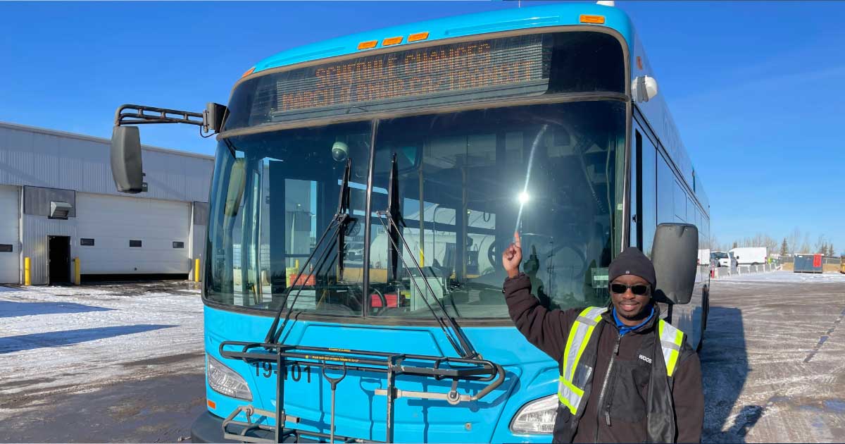 A RMWB Transit operator points to a digital sign that reads Schedule Changes March 8 rmwb.ca/transit
