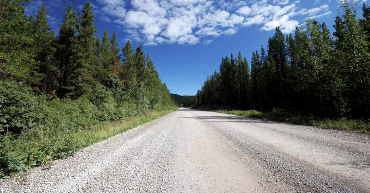 Wide gravel road cutting through northern Canadian forest.