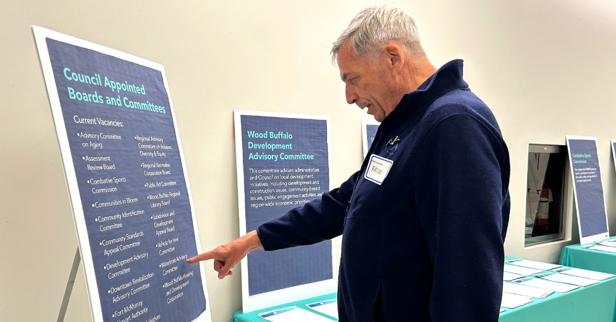 A Council-appointed committee member points to a board displaying municipal committees in Fort McMurray, Alta.