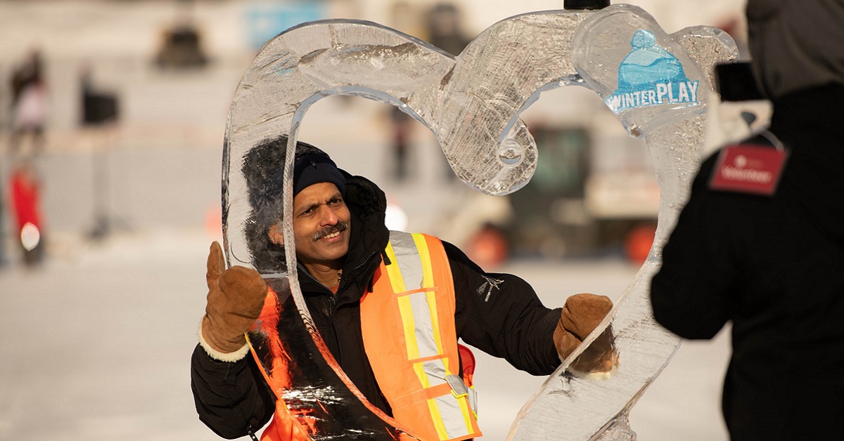 A volunteer takes a moment to pose with an ice sculpture at WinterPLAY.