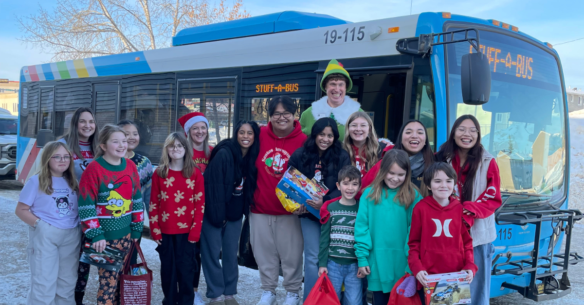 Santas Anonymous students pose with Buddy the Elf and elementary school students during the Stuff-A-Bus toy drive