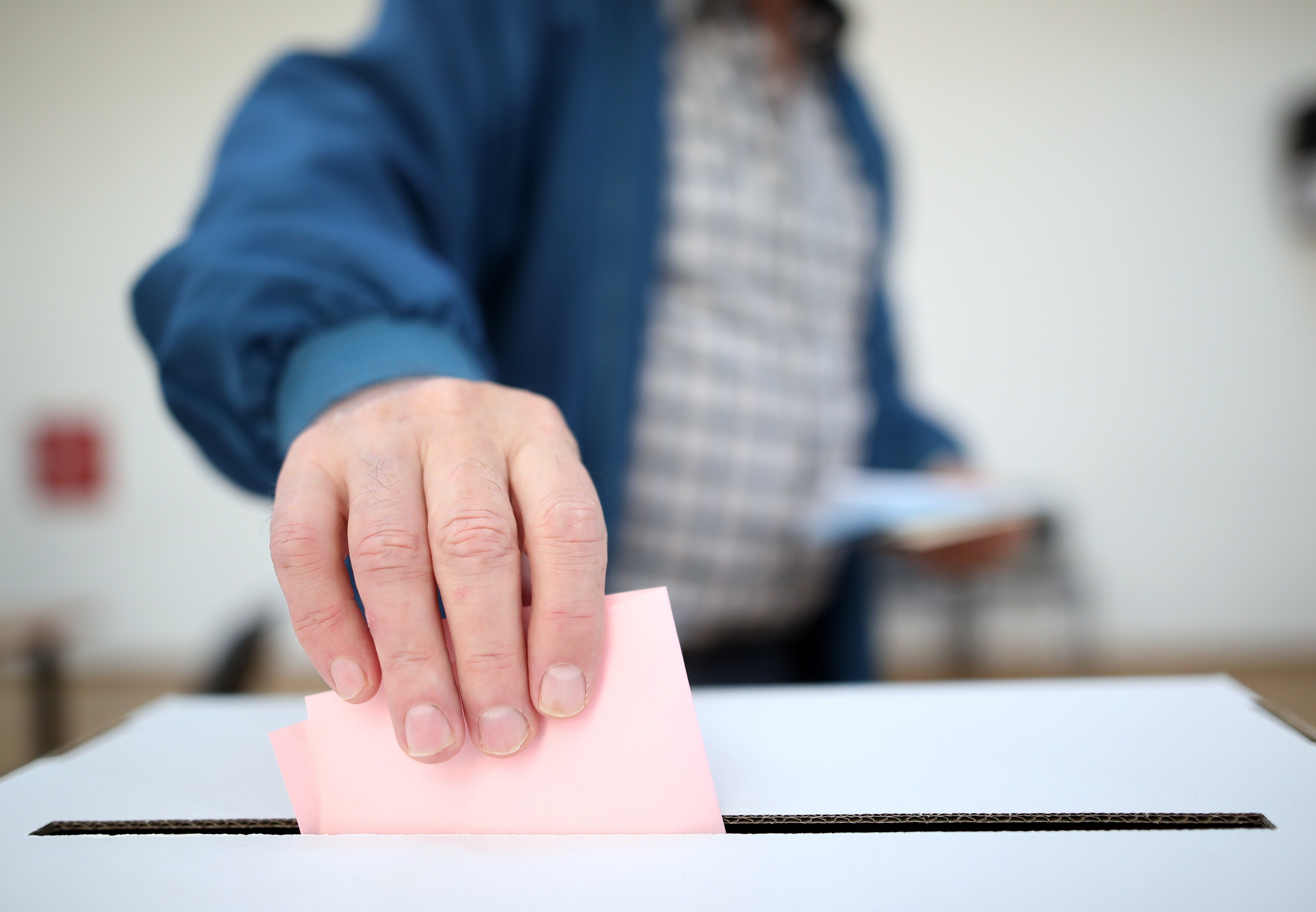 A hand places a ballot in a box.