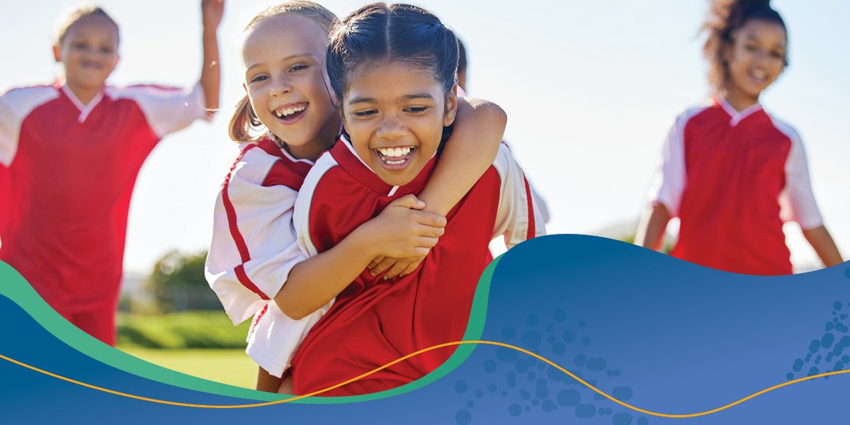 Picture of young girls playing soccer and two are hugging.