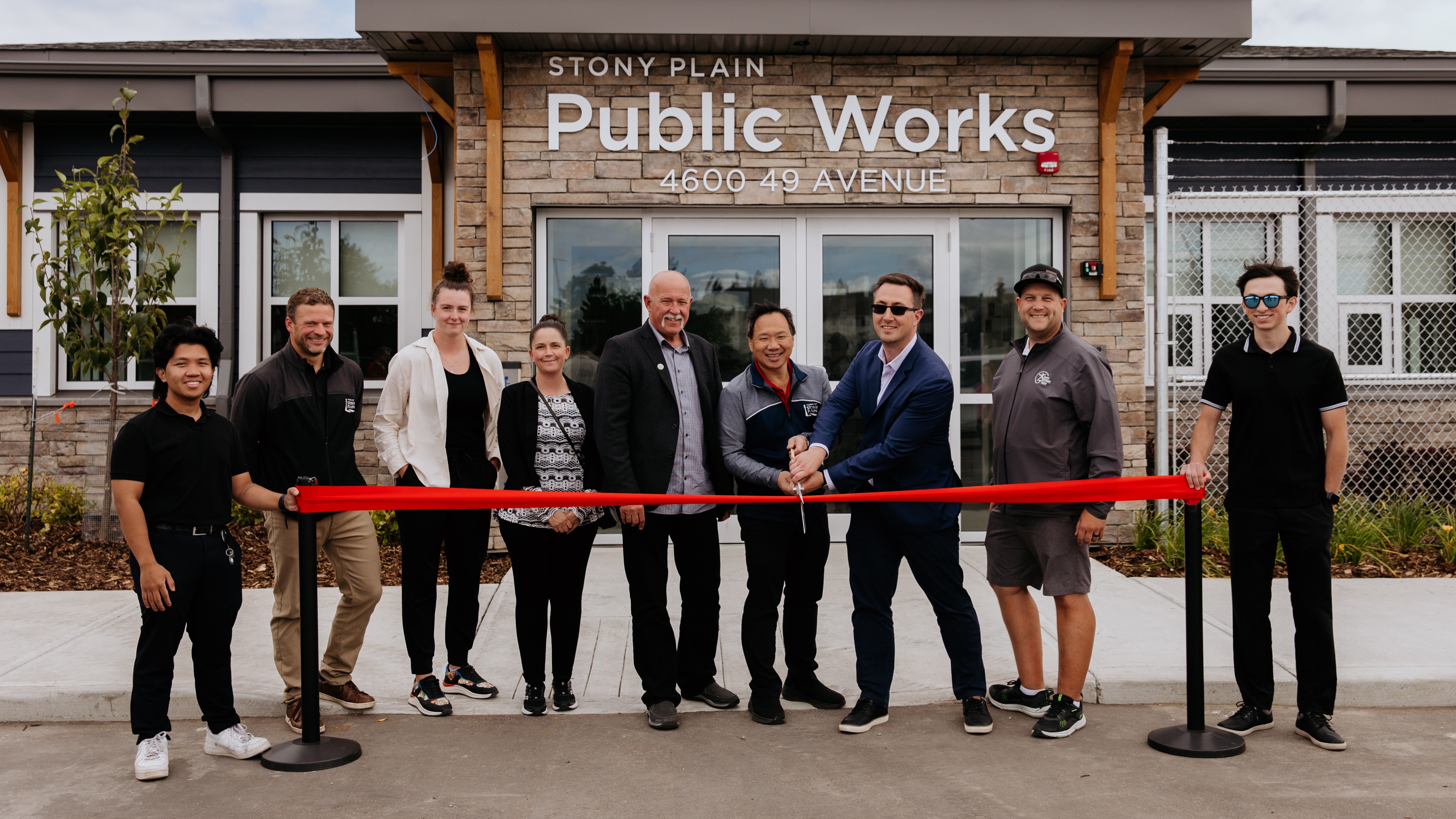 image of Mayor and Council cutting a red ribbon with large gold scissors in front of a brick building that reads, "Stony Plain Public Works"