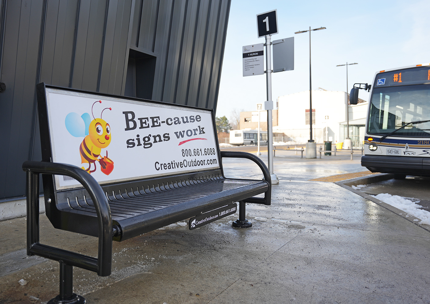 Bench advertisement with illustration of a bee. Text reads "Bee-cause signs work"