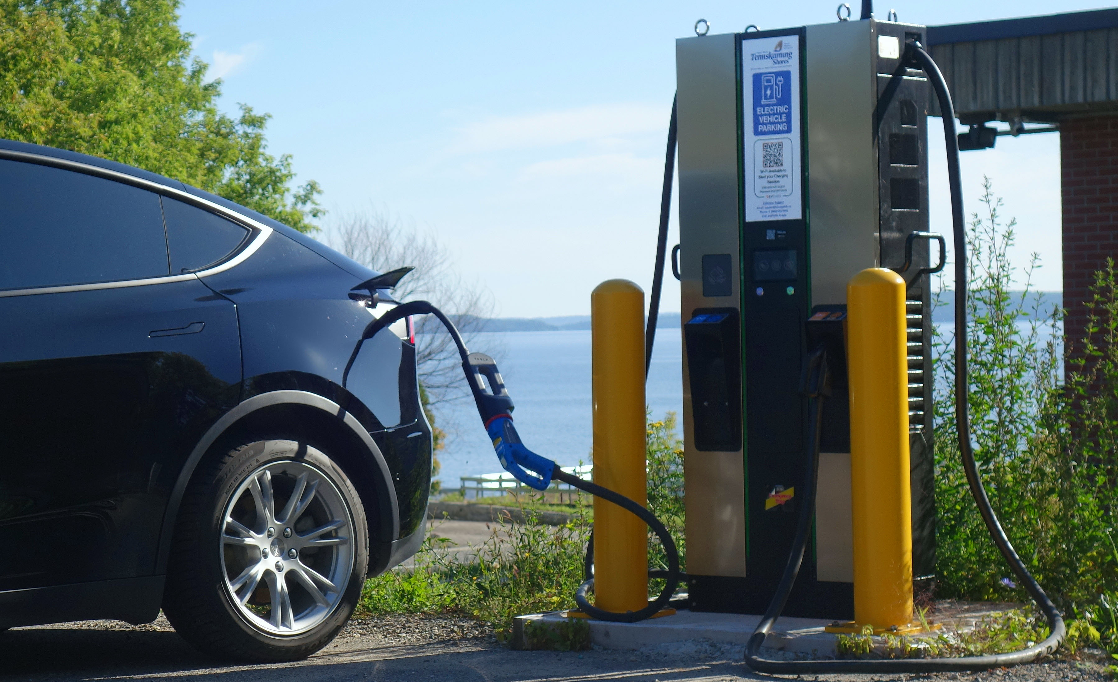 Electric vehicle charging at the Haileybury beach EVStart Charging Station in Temiskaming Shores, Ontario, with Lake Timiskaming in the background on a summer day