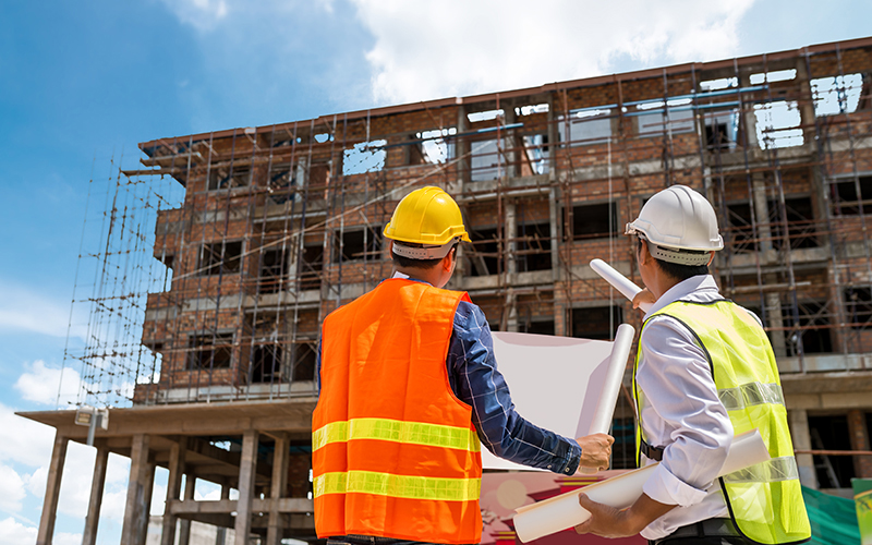 Two workers looking over plans in front of a building under construction