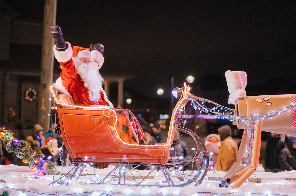 Santa Claus with arms raised sitting in a sleigh on a parade float