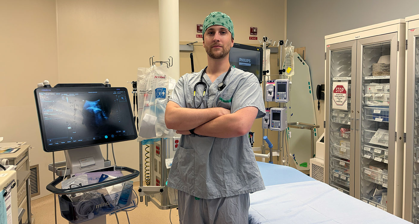 Joshua stands in front of a stretcher in a Emergency Department exam room