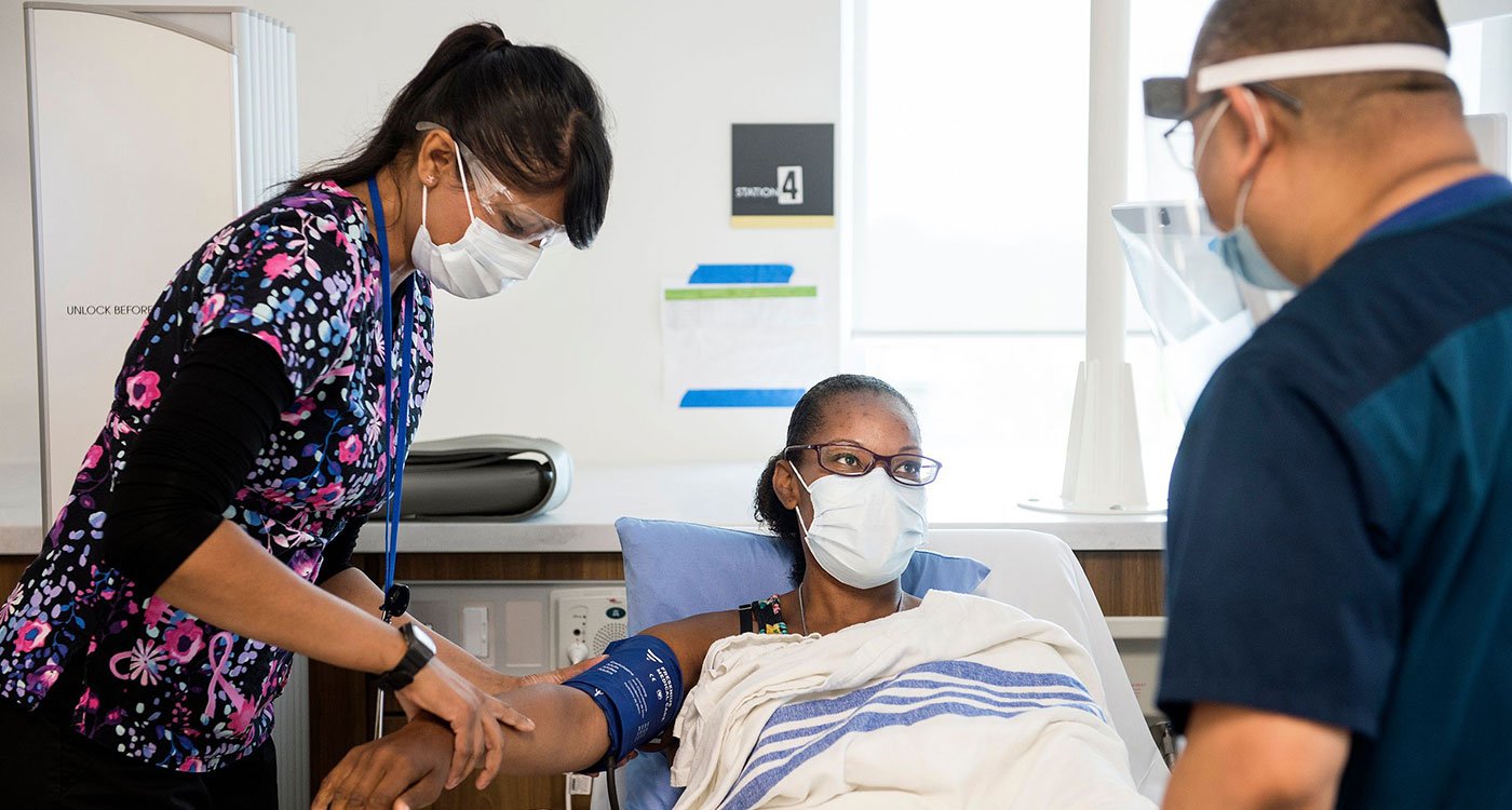 Two clinical staff members assist a patient with checking her heart rate