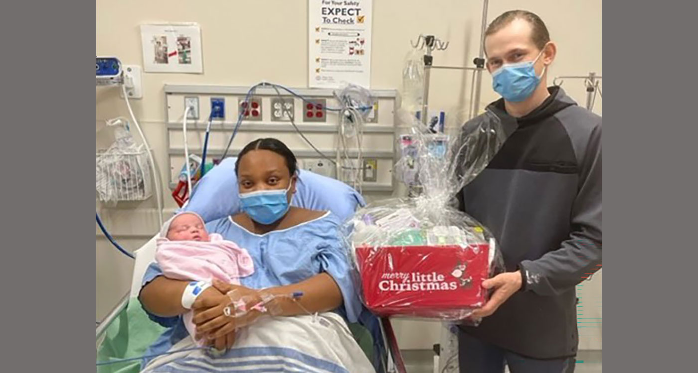(l-r): Teshanda Gilling holds baby girl while lying in bed with Blake Sedore standing beside